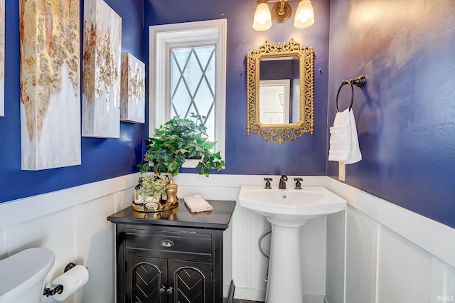 half bath with wainscoting, toilet, and a sink