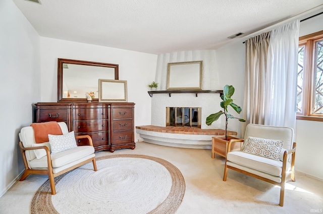 living area featuring visible vents, a brick fireplace, baseboards, carpet flooring, and a textured ceiling