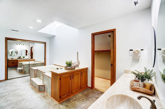 full bath with visible vents, vanity, a skylight, a bath, and a textured ceiling