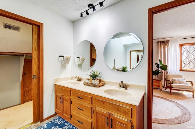 bathroom featuring a sink, visible vents, a textured ceiling, and double vanity