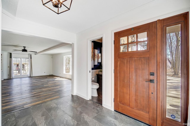 entryway featuring stone finish floor, ceiling fan with notable chandelier, and baseboards