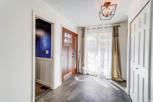 entryway with a notable chandelier, wainscoting, and a textured ceiling