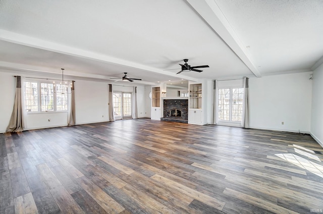 unfurnished living room with wood finished floors, baseboards, a fireplace with raised hearth, beamed ceiling, and ceiling fan with notable chandelier