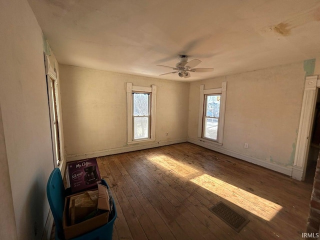 empty room with hardwood / wood-style flooring, a ceiling fan, visible vents, and baseboards