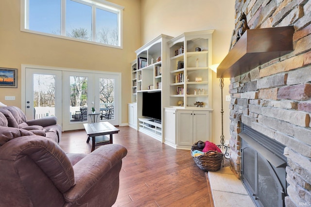 living area with french doors, a high ceiling, a stone fireplace, and wood finished floors