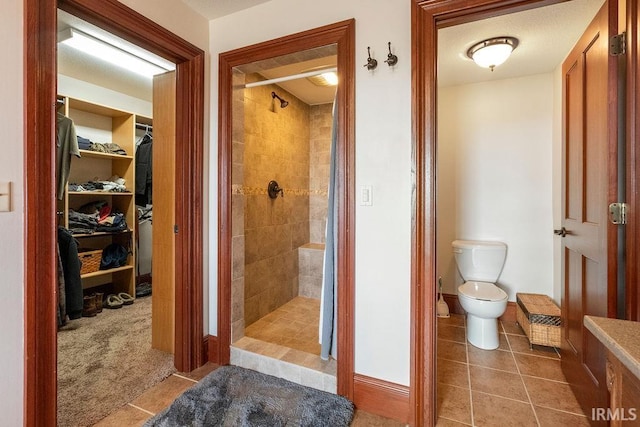 bathroom featuring tile patterned floors, toilet, a stall shower, and a spacious closet