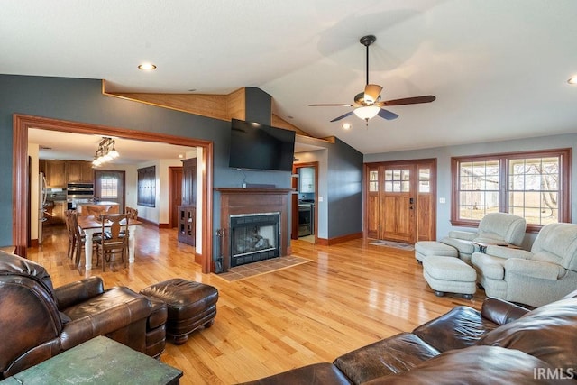 living room featuring light wood-style flooring, lofted ceiling, ceiling fan, and a fireplace with flush hearth