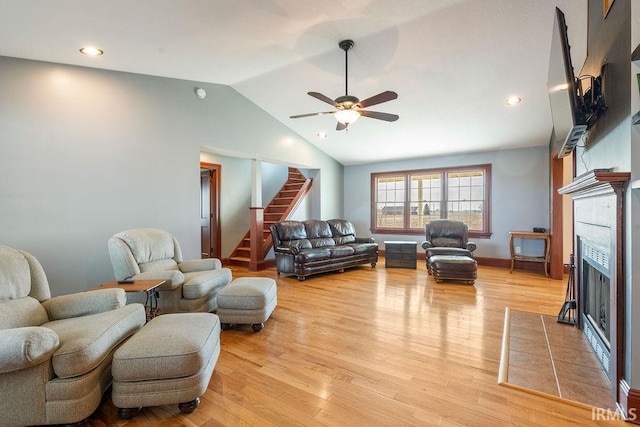 living room with a ceiling fan, light wood finished floors, lofted ceiling, stairs, and a tiled fireplace