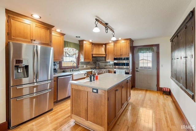 kitchen with custom exhaust hood, stainless steel appliances, light countertops, light wood-type flooring, and backsplash