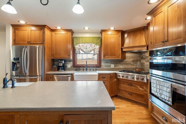 kitchen with brown cabinetry, a sink, appliances with stainless steel finishes, and premium range hood