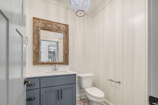 half bath featuring a notable chandelier, toilet, vanity, and baseboards