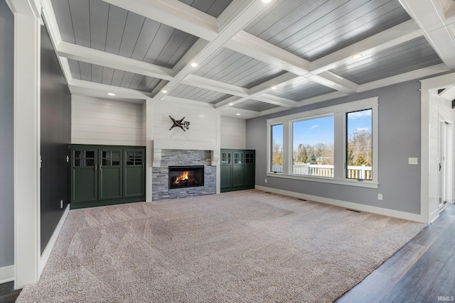 unfurnished living room with visible vents, baseboards, coffered ceiling, a stone fireplace, and beamed ceiling