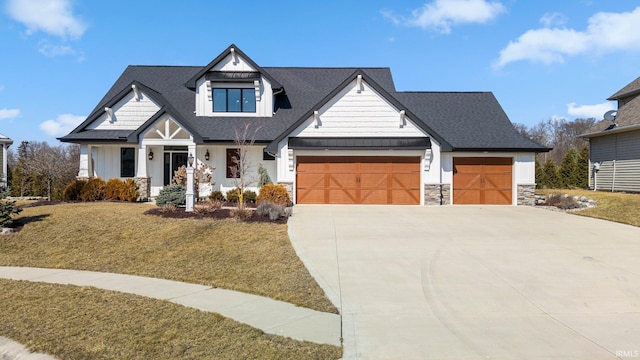 modern farmhouse with a shingled roof, a front yard, driveway, stone siding, and an attached garage