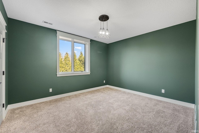 carpeted spare room featuring baseboards, visible vents, and a textured ceiling