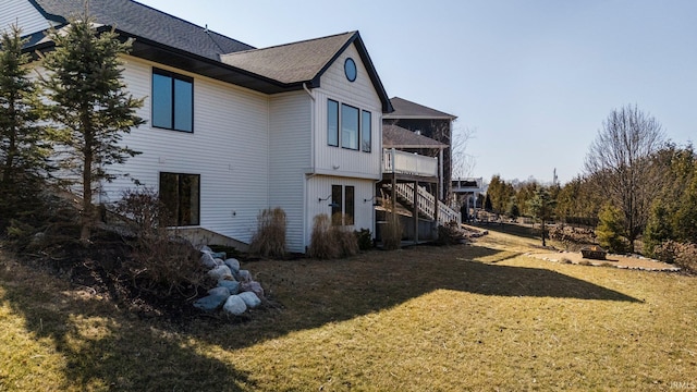 back of property featuring stairs, a lawn, and roof with shingles