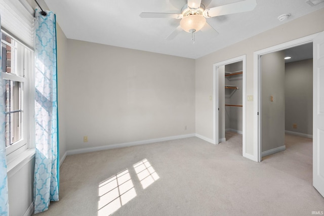 unfurnished bedroom with a walk in closet, multiple windows, light colored carpet, and baseboards