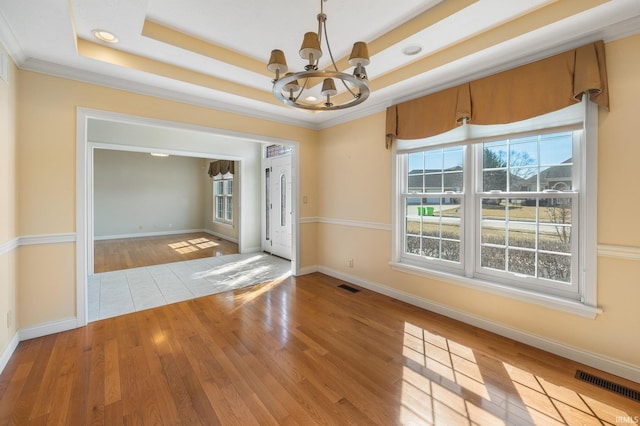 unfurnished room with a notable chandelier, visible vents, a raised ceiling, and wood finished floors