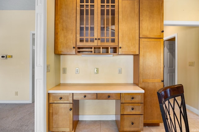 kitchen featuring light countertops, light tile patterned flooring, glass insert cabinets, and built in desk