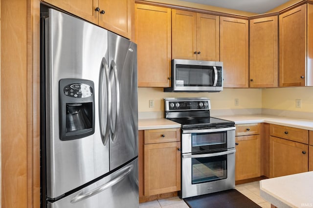 kitchen featuring light tile patterned floors, appliances with stainless steel finishes, brown cabinetry, and light countertops