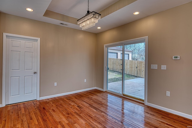 spare room with visible vents, wood finished floors, baseboards, and a chandelier