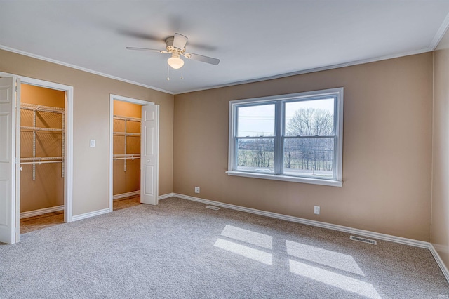 unfurnished bedroom featuring visible vents, a ceiling fan, carpet, crown molding, and baseboards