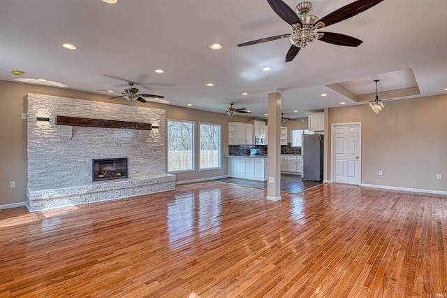 unfurnished living room with a stone fireplace, light wood-style flooring, baseboards, and ceiling fan