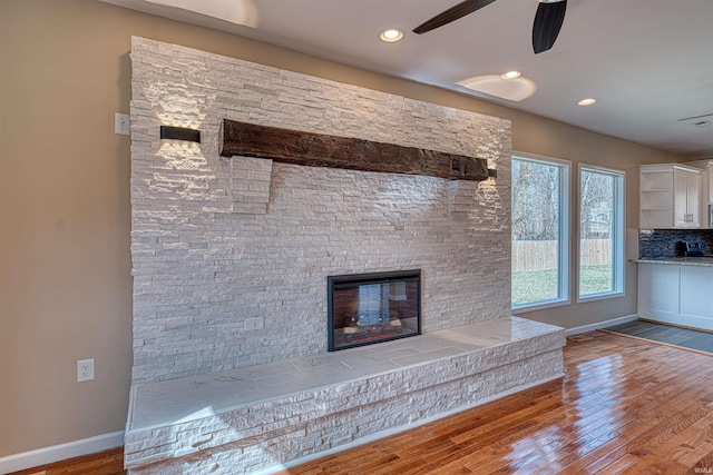 unfurnished living room with a glass covered fireplace, wood finished floors, baseboards, and a ceiling fan