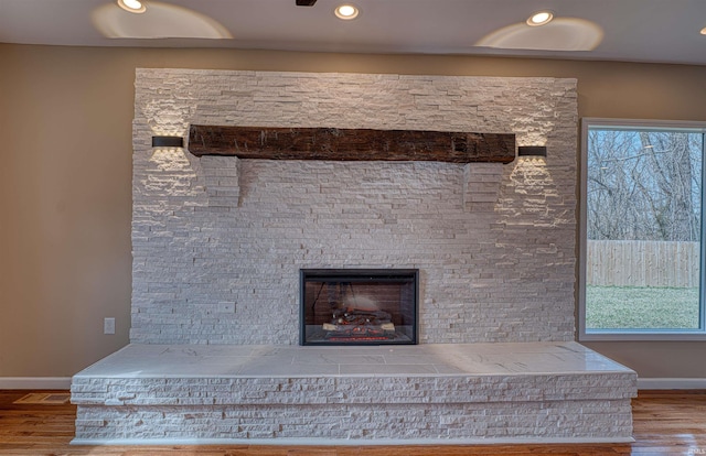 interior details featuring a glass covered fireplace, baseboards, wood finished floors, and recessed lighting