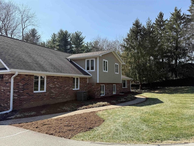 view of side of home featuring a yard, brick siding, and a shingled roof