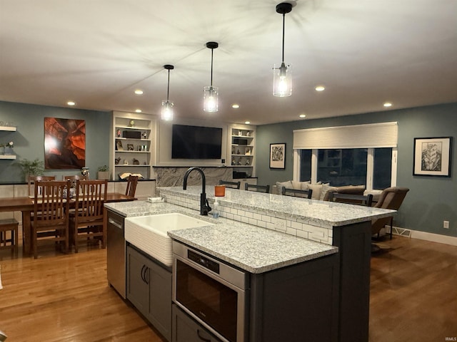 kitchen featuring a sink, open floor plan, stainless steel dishwasher, wood finished floors, and a kitchen island with sink