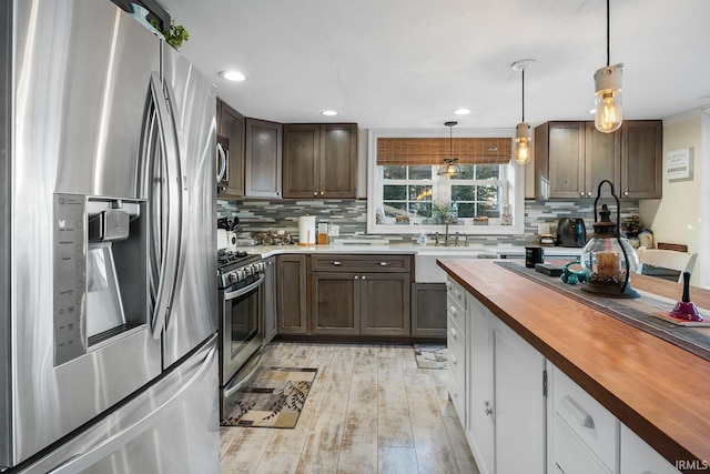 kitchen featuring decorative light fixtures, decorative backsplash, appliances with stainless steel finishes, light wood-style floors, and wood counters