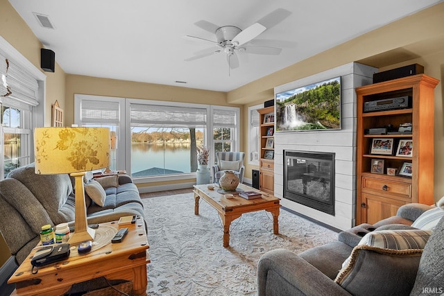 living area with a glass covered fireplace, a ceiling fan, and visible vents