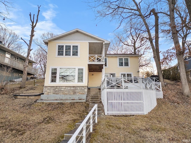 rear view of property with a balcony, stone siding, and a wooden deck