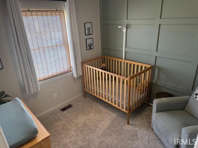 carpeted bedroom featuring a crib, a decorative wall, baseboards, and visible vents