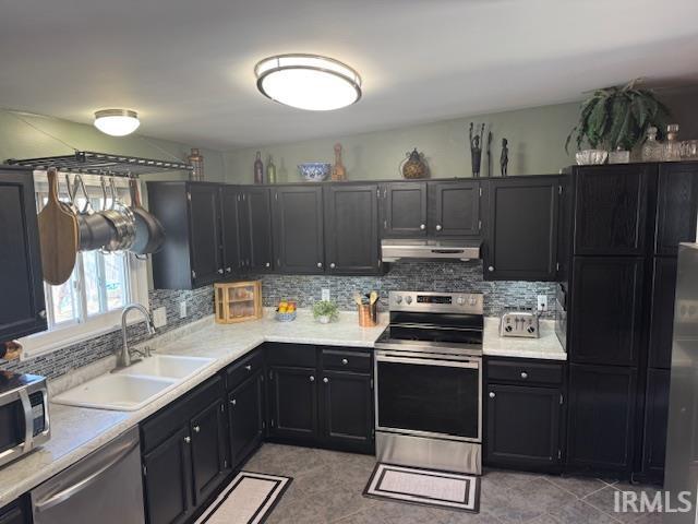 kitchen with tasteful backsplash, under cabinet range hood, appliances with stainless steel finishes, dark cabinetry, and a sink