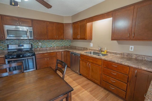 kitchen with light wood-style flooring, a sink, stainless steel appliances, brown cabinetry, and decorative backsplash