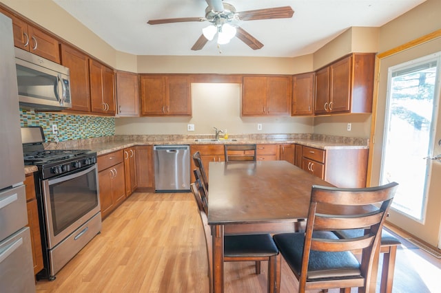 kitchen with a ceiling fan, brown cabinetry, a sink, light wood-style floors, and appliances with stainless steel finishes