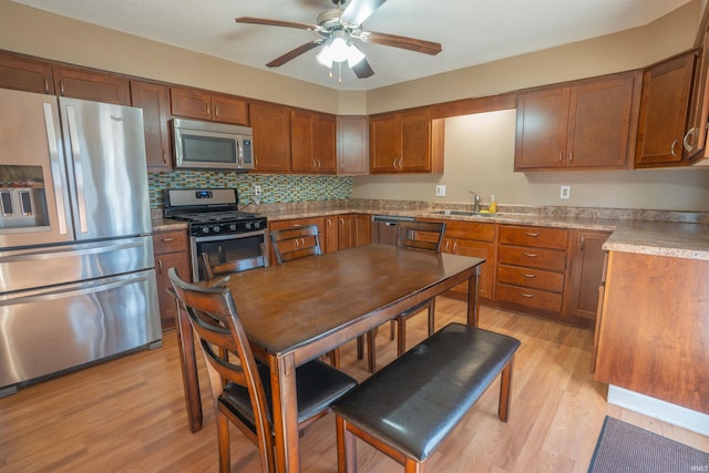 kitchen featuring a ceiling fan, a sink, stainless steel appliances, light wood-style floors, and brown cabinets