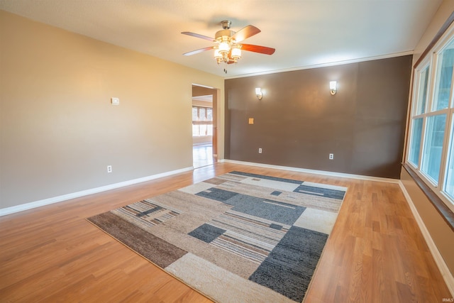 empty room featuring baseboards, crown molding, a ceiling fan, and wood finished floors