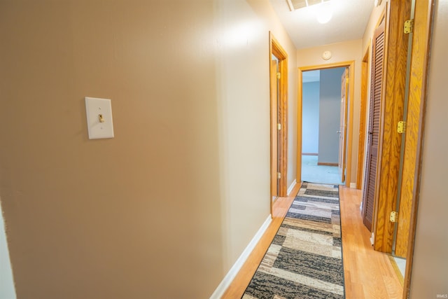 hallway featuring light wood finished floors, visible vents, and baseboards