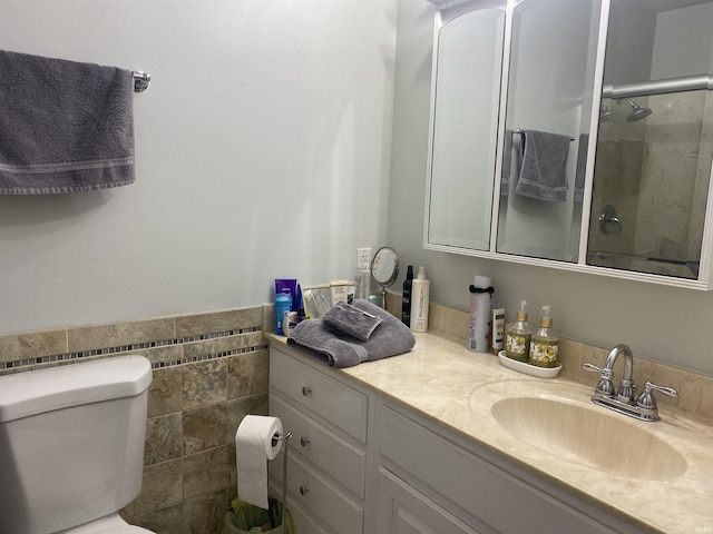 bathroom with vanity, wainscoting, tile walls, toilet, and a shower with door