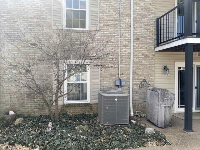 view of home's exterior with brick siding, central AC unit, and a balcony