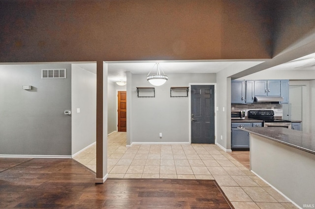 kitchen with visible vents, under cabinet range hood, light tile patterned floors, decorative backsplash, and stainless steel range with electric cooktop