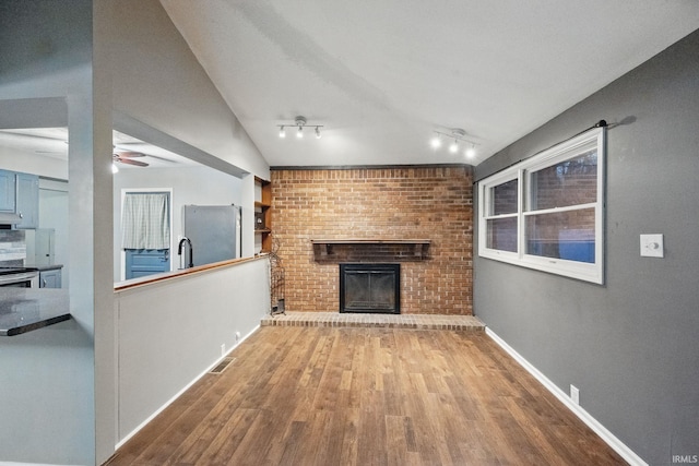 unfurnished living room featuring a ceiling fan, a brick fireplace, wood finished floors, and visible vents