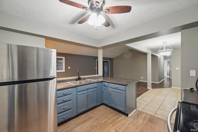 kitchen with range with electric cooktop, a sink, blue cabinetry, freestanding refrigerator, and a peninsula