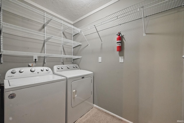 clothes washing area with baseboards, light colored carpet, laundry area, washer and dryer, and a textured ceiling