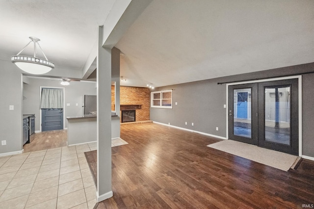 unfurnished living room featuring baseboards, a brick fireplace, ceiling fan, and light wood finished floors