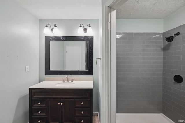 full bath featuring a tile shower, a textured ceiling, and vanity