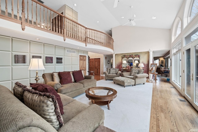 living area featuring visible vents, decorative columns, light wood-style flooring, a towering ceiling, and a ceiling fan