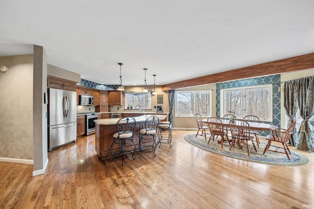 kitchen featuring light wood-style flooring, light countertops, appliances with stainless steel finishes, a kitchen bar, and brown cabinets